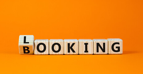 Looking and booking symbol. Turned the wooden cube and changed the word 'looking' to 'booking'. Beautiful orange background, copy space. Business, looking and booking concept.