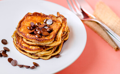 White plate with egg pancakes with chocolate pieces and pink background.