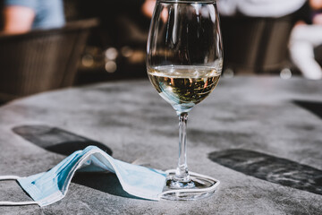 Wine glass and face mask on a table. Measures in outdoor cafe, bar or restaurant after reopening after quarantine.