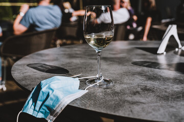 Wine glass and face mask on a table. Measures in outdoor cafe, bar or restaurant after reopening after quarantine.