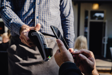 Contactless payment system, close-up. Client man paying bill by phone in outside restaurant, bar or cafe.