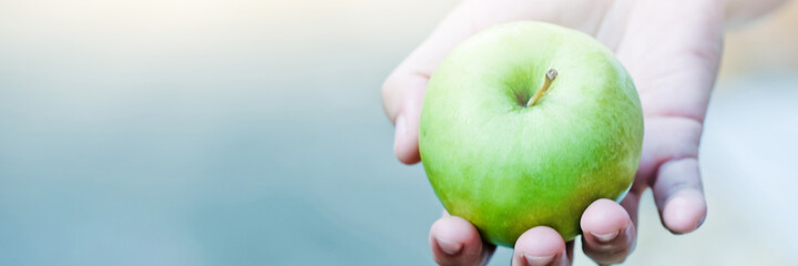 Young Girl hand holding Green Apple on beautiful blur Background.
