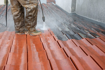 Half finished washing of rooftop from dirt and lichen. Professional is using special equipment to remove dirt from roof tiles. © Branimir
