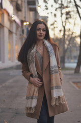 Obraz premium A girl in a brown coat and a blouse, the evening city is behind her.