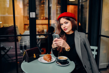 Female blogger chatting with followers in social networks on modern smartphone using 5G internet connection.Hipster girl in watching video on website on cellular in cafe.