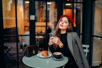 Female blogger chatting with followers in social networks on modern smartphone using 5G internet connection.Hipster girl in watching video on website on cellular in cafe.