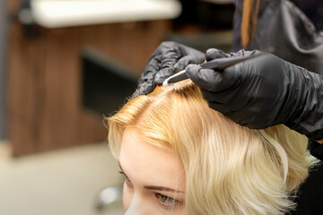 Fototapeta premium A closeup head of a young blonde woman receiving dyeing hair in a hair salon