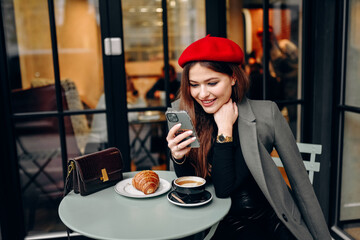 Female blogger chatting with followers in social networks on modern smartphone using 5G internet connection.Hipster girl in watching video on website on cellular in cafe.