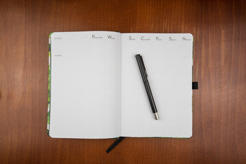 Top view of an open empty weekly dairy planner with a pen on a wooden table