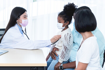 Asian woman doctor wearing surgical mask and using a stethoscope, checking the respiratory system and heartbeat Of a 5-year-old girl, who is half African half Thai, to family and  health care concept.
