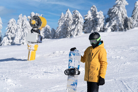 A snowboarder in a yellow jacket poses on the track with a snowboard