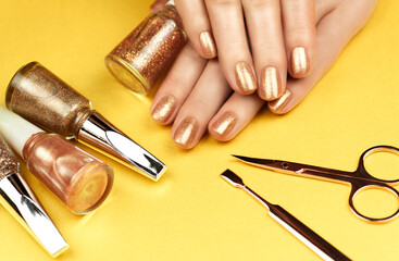 Woman making manicure by herself. Female hands with bronze-colored manicure on a shiny bronze background.