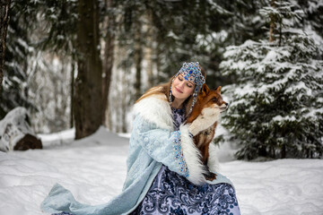 beautiful Russian girl in a winter national dress with a red fox in a winter snowy forest 