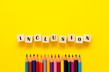 Inclusion concept word on wooden cubes and pencils on yellow background