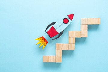 Wood block step stairs and colorful rocket on blue background. Business concept for growth success...