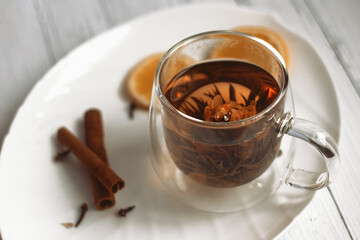 The tea flower is brewed, opened in a transparent cup on a white platter, with cinnamon and cloves