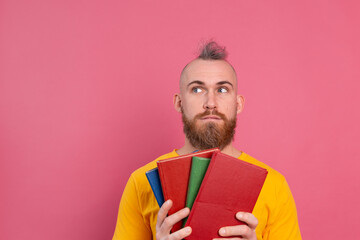 Adult smiling casual clothes guy with beard hugs favorite books to himself isolated on pink background