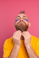European handsome bearded man in yellow t-shirt and purple eye patches mask, face care for men. Isolated on pink background.