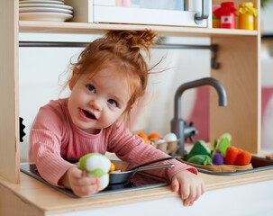 cute toddler baby girl playing on toy kitchen at home - obrazy, fototapety, plakaty