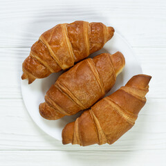 Plate of fresh baked croissants on white wooden table top view