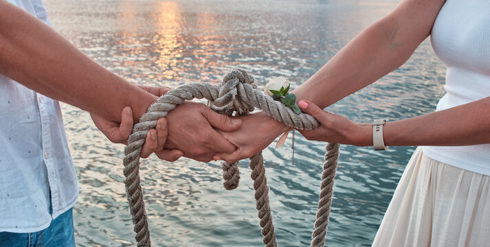 Wedding ceremony handsbye, wedding anniversary, valentine's day tied in nautical rope handfasting vows, as a sign of eternal love and veneration. Young hands are tied with a carrot with a rope as a