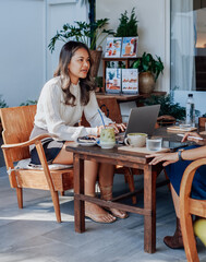 Asian serious businesswoman discuss something with her coworker sitting at table outside and using a laptop in cafe.