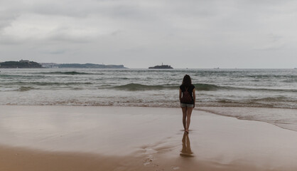 Alone girl in a beautiful and cloudy beach day with reflection water, Cantabria, Spain