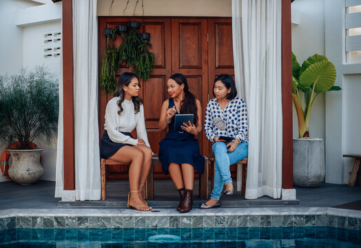 Professional occupation of three asian women they discuss and planning their project using a tablet near swimming pool in mansion.