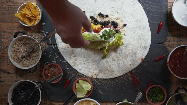 Making a traditional Mexican cuisine dish burrito on the table. Top down view of food preparation on the table. Wrapping up and cutting burrito in half