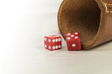 Red dices with dice cup on a white wooden table.