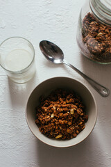 Chocolate granola for breakfast. A jar and and a bowl of muesli and glass of yoghurt