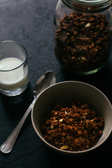 Chocolate granola for breakfast. A jar and and a bowl of muesli and glass of yoghurt