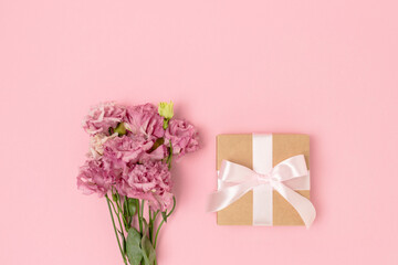Gift box with a tied bow and bouquet of eustoma flowers on a pink background. Present for Mothers Day with copyspace.