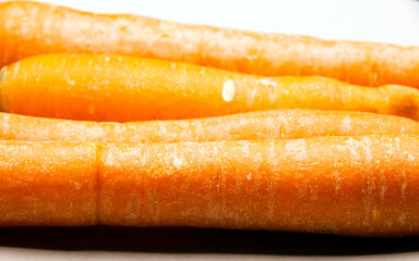Four raw organic carrots on a white porcelain plate closeup