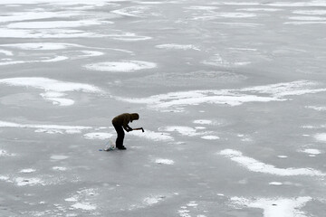 The man is chopping thin ice. Danger of winter fishing.