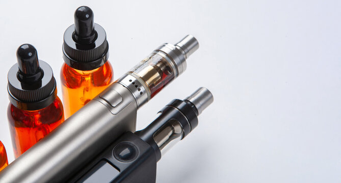 Silver and black vapes next to the vials. Liquids for electronic cigarettes. Smoking e-cigarettes. Vaping accessories. Devices for Smoking electronic cigarettes.