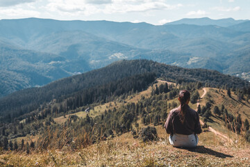 Naklejka premium Young woman sitting on a rock with backpack and looking to the horizon
