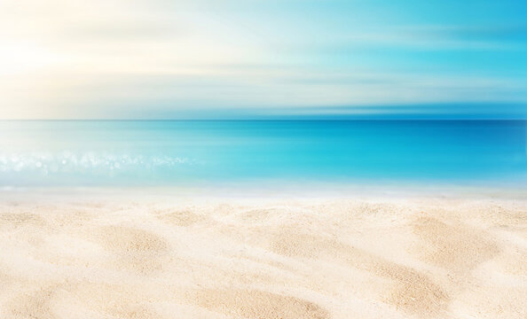 Summer background image of tropical beach with blurred horizon at sunset. Light sand of beach against backdrop of sparkling ocean water. Natural seascape.