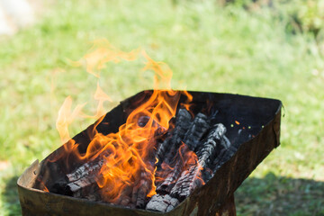 defocused orange flame of a campfire for barbecue in summer on green grass background