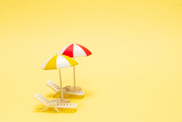 Two sun loungers and a red umbrella on a yellow background.