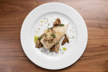 Beautifully cooked fried squid carcass with wild mushrooms and herbs in a white plate on a wooden table. Top view.