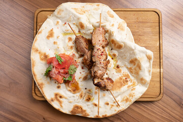 Hot beef kebab with tomatoes, onions and freshly baked tortilla on a wooden cutting board. Traditional Eastern halal dish of beef, veal or lamb grilled on the grill.
