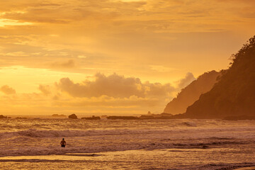 Unrecognizable man, in the water watching the sunset on a beach in Costa Rica