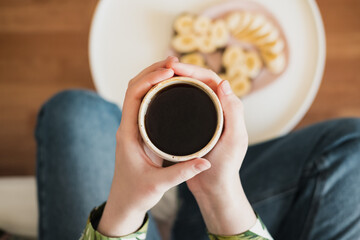 Woman holds a cup of black coffee, shot directly above. Having breakfast, drinking morning coffee...