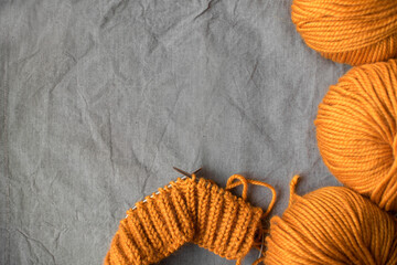 Fototapeta na wymiar bright balls of orange woolen thick yarn and knitting on a gray wrinkled background with place for text