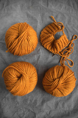 bright balls of orange woolen thick yarn and knitting on a gray wrinkled background with place for text