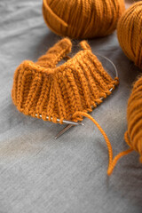 bright balls of orange woolen thick yarn and knitting on a gray wrinkled background with place for text