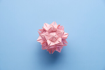 Pink handmade modular origami ball or Kusudama Isolated on blue background. Visual art, geometry,...