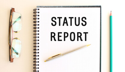 Notepad with text STATUS REPORT on a white background, near glasses and pencil.