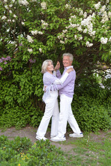 portrait of beautiful senior couple dancing  by lilacs in the park